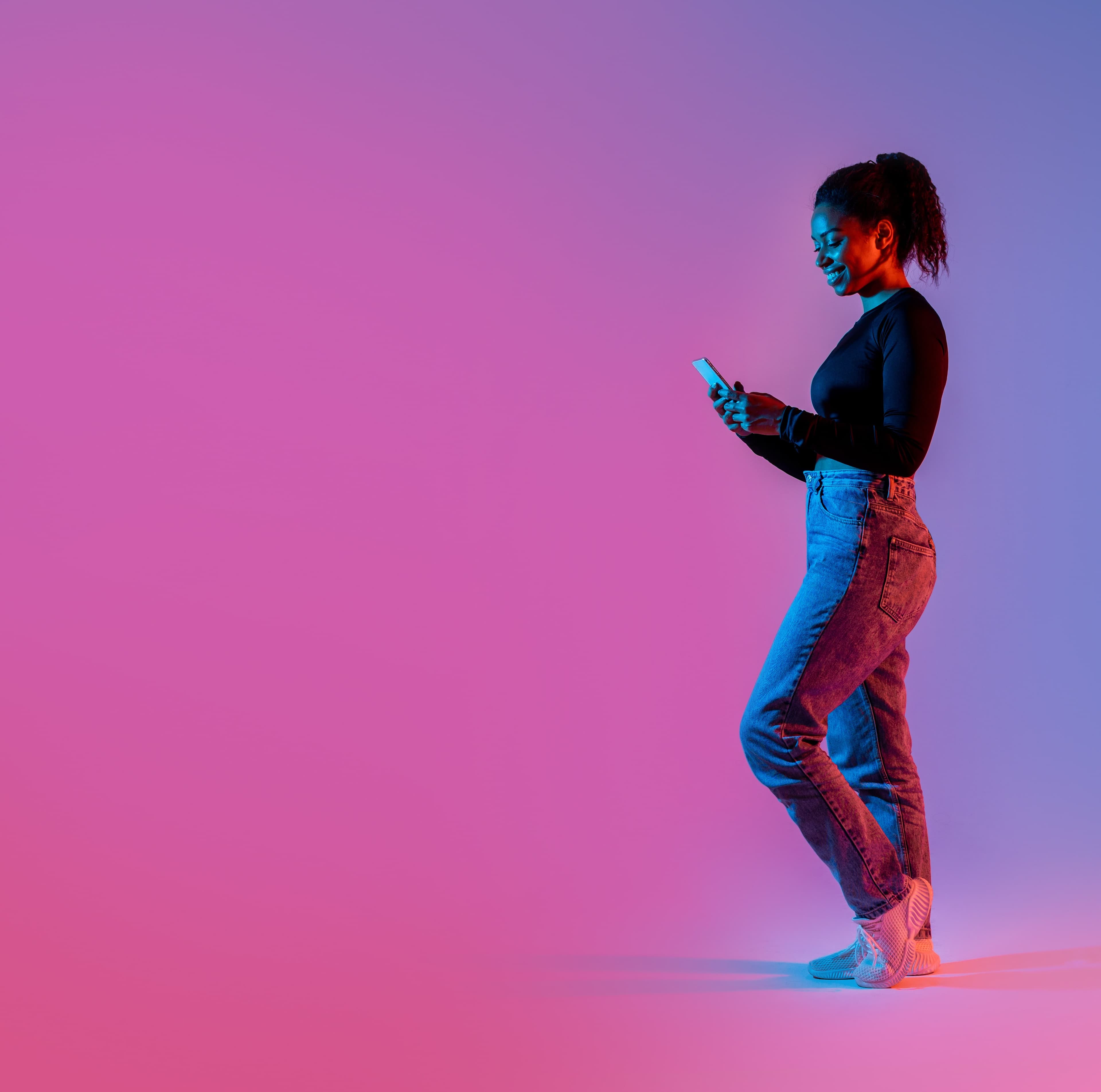 A smiling woman looking at her phone with a neon background.